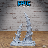 Two bone spike terrain pieces assembled together on a shared skull-strewn rubble base — one taller upright spire and one smaller leaning spike — showing the multipart arrangement. Sculpt by Epic Miniatures.