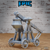 Trebuchet terrain model with spiked wheels, rotating throwing arm angled upward, hopper counterweight, and iron-bolted timber frame on a wheeled base. Sculpt by Epic Miniatures.