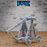 Trebuchet terrain model showing the throwing arm raised at a steep angle, torsion spring mechanism visible at the base, spiked wheels, and crossed timber support structure. Sculpt by Epic Miniatures.