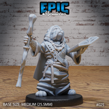Stocky canine humanoid wizard facing forward, raising a bone-topped staff in one hand and holding an open spellbook in the other, wearing a rope-belted patchwork robe with bead necklaces. Sculpt by Epic Miniatures.