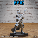 Female dark elf soldier gripping a long spear diagonally across her body, wearing spiked plate armour, sculpted pauldrons, and a crested pointed helm. Long cloak sweeps behind her legs. Sculpt by Epic Miniatures.