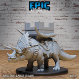 Armoured triceratops war-beast with plated shoulder guards, skull harness ornament, and cord-bound legs, carrying a crenellated timber howdah lashed across its back. Sculpt by Epic Miniatures.