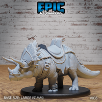 Armoured triceratops miniature viewed from the front-left, showing three prominent horns, spiked frill barding, full riding saddle with rolled pack, rope detailing, and ankle wraps. Sculpt by Epic Miniatures.