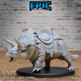 Armoured triceratops miniature in a lowered charging stance, wearing a fitted frill armour plate, rope-wrapped leg wraps, and a detailed padded saddle with scrolled cantle. Sculpt by Epic Miniatures.