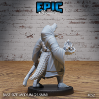 Alligator-headed robed spellcaster seen from behind, powerful scaled tail prominent, one clawed hand raised with splayed fingers as if channelling energy, dagger sheathed at the back. Sculpt by Epic Miniatures.