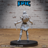 Hobgoblin female miniature seen from behind, showing a voluminous braided fur cloak cascading down the back, dual daggers held low at each side, wrap-bound legs and spiked pauldrons. Sculpt by Epic Miniatures.