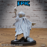 Hobgoblin female sorcerer seen from behind, large billowing cloak dominating the silhouette with worn fabric detail, runic gauntlet arm raised above the hood, armoured legs visible below the cape hem, cobblestone rubble base. Sculpt by Epic Miniatures.