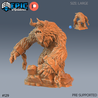 Unpainted orange resin 3D printed large yeti miniature from Epic Miniatures, shown in three-quarter front view. The creature is heavily furred with layered shaggy texture, has two curved horns, iron shackle cuffs on both wrists, a snarling open-mouthed expression, and crouches forward over a craggy rock base. A small-scale painted version and blue d20 are visible in the upper right corner for size reference.