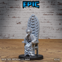 Robed shaman elder seated on a tall ceremonial throne, chin resting on one raised hand, wearing a fan-shaped headdress and layered bead necklaces, a skull resting at the throne's base. Sculpt by Epic Miniatures.