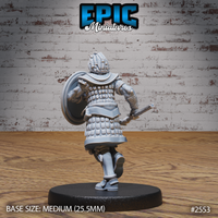 Scale-armoured warrior seen from behind in a running pose, round shield strapped to the left arm, short blade in the right hand, overlapping scale detail visible across back and hips, by Epic Miniatures.
