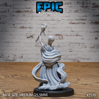 Female spellcaster seen from behind with one arm raised high holding a skull-topped staff, long flowing robes pooling around the base, wrapped hair visible, wide shoulder collar detailed across the back. Sculpt by Epic Miniatures.