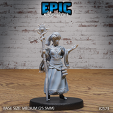 Female seer standing upright, raising a tall staff crowned with a spiked sun-orb totem, opposite arm extended with spread fingers. Wrapped turban, layered robes with geometric hem border, jewelled necklace. Sculpt by Epic Miniatures.