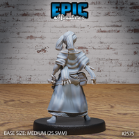Female tribal seer shown from behind, revealing a belt hung with bone or tooth fetishes and a quiver-like arrangement of spears at her back. Wrapped turban and layered robe with decorative trim visible. Sculpt by Epic Miniatures.