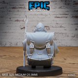 Hamster monk seen from behind, showing a large buckled travel pack across broad shoulders, a flowing robe with deep fabric folds, and the wooden staff extending upward beside him. Round cap visible at the top of the head. Sculpt by Epic Miniatures.