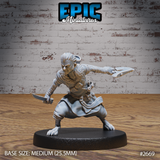 Halfling skin changer in a wide combat crouch, snarling expression, dagger in one hand and forked blade weapon extended forward, wearing a fur collar and wrapped forearms. Sculpt by Epic Miniatures.