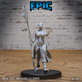 Lizardfolk female warrior striding forward, holding a tall ornate polearm in one raised hand with the other hand curled as if channelling power. Wrapped cloth armour, small head horns, bare feet. Sculpt by Epic Miniatures.