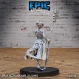 Lizardfolk female warrior seen from the side, weight shifted onto one leg with the other raised mid-stride. Tall ritual polearm angled back, layered cloth armour with a split battle-skirt, small curved horns. Sculpt by Epic Miniatures.