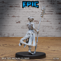 Lizardfolk female warrior seen from the side, weight shifted onto one leg with the other raised mid-stride. Tall ritual polearm angled back, layered cloth armour with a split battle-skirt, small curved horns. Sculpt by Epic Miniatures.