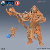 Digital render of an unpainted hobgoblin shaman miniature in 32mm scale, shown alongside a d20 for size reference. The character is broad and muscular, wearing layered ornate tribal armour with a detailed belt medallion. He holds a large gnarled branching staff aloft in one hand with his arm outstretched, teeth bared in a snarl. Sculpted by Epic Miniatures.