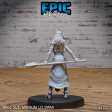 Female wizard in layered plate armour seen from behind, long hair falling to mid-back, gripping a crystal-tipped staff horizontally at waist height, skirt flowing to armoured greaves. Sculpt by Epic Miniatures.