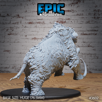 Rear three-quarter view of the same unpainted grey resin woolly mammoth miniature — showing the heavily detailed shaggy fur across the back and haunches, bony ridge spines along the spine, rear legs driving forward mid-charge, on a 76.5mm oval base. Epic Miniatures sculpt #3602.