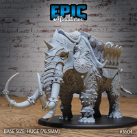 Unpainted grey resin war mammoth miniature on a 76.5mm Huge base, shown from the front-left angle. The mammoth wears full spiked iron barding with bladed tusk-caps, layered armour plates across its legs and face, and a detailed howdah loaded with crossbow racks and shield rails. A cloaked rider figure is visible at the front of the platform.