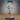 Unpainted grey resin 32mm miniature of a tribal female archer mid-stride, feathered and horned headdress, bow drawn and aimed, skull trophy at her belt, feather-and-hide mantle, dynamic swirling flame base — front view