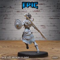 Rear view of the same unpainted grey resin tribal female warrior miniature, showing the detail of her feathered headdress, layered pelt cloak, and an ornate spear with a carved haft and beast-tooth tip, mounted on a medium round black base — by Epic Miniatures