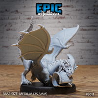 Unpainted grey resin White Dragon Wyrmling miniature by Epic Miniatures, front-three-quarter view showing the wyrmling in a low bite pose clutching a skull trophy in its jaws, wings flared wide, scaled body and ridged horn visible, on a medium 25.5mm black base