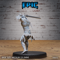 Rear three-quarter view of the same unpainted grey resin Cave Elf Barbarian miniature by Epic Miniatures, showing detailed chainmail texture on the hip wrap, braided shoulder hair, and the full extension of the greatsword arm driving the blade forward, on a medium 25.5mm black base