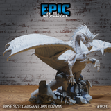 Unpainted grey resin Glacier Dragon miniature by Epic Miniatures, front three-quarter view — gargantuan dragon on a 102mm base crouching atop shattered rock, wings spread wide, one foreclaw raised, with detailed ridge scales, feathered wing membranes, and hooked wing tips