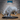 Unpainted grey resin woolly rhino miniature by Epic Miniatures, photographed from the front-left — head lowered in a charging pose, shaggy layered fur texture across the full body, two curved horns prominent, hooves resting on a shattered ice scatter base, mounted on a large 51mm oval black base