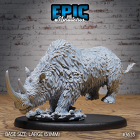 Unpainted grey resin woolly rhino miniature by Epic Miniatures, photographed from the front-left — head lowered in a charging pose, shaggy layered fur texture across the full body, two curved horns prominent, hooves resting on a shattered ice scatter base, mounted on a large 51mm oval black base