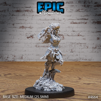 Unpainted grey resin orc female barbarian miniature in 32mm scale, shown from the front — mid-battle cry with mohawk hair and bone braids, raising a skull-adorned axe overhead, belt hung with skull trophies, standing on a scenic base of skulls and bones