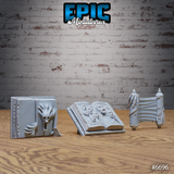 Three unpainted grey resin scatter terrain pieces from Epic Miniatures: a closed tome with a screaming beast embossed on the cover, an open grimoire on a reading stand with anguished faces carved into the pages, and a ceremonial scroll bound around ornate spindles — photographed on a wooden surface against a brick wall background.