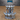 Front view of an unpainted grey resin Blood Fountain terrain piece by Epic Miniatures — a two-tiered dark shrine with a spiked upper crown, weeping skulls, and an ornate carved face on the stone base, printed by Mitz and Simz