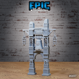 Unpainted grey resin bell tower terrain miniature with skeletal figures in hanging cage-lanterns and alcoves, featuring an ornate bell on a four-pillared stone arch structure with crenellated towers — front three-quarter view