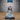 Unpainted grey resin miniature of an Experienced Lich by Epic Miniatures — front view showing skeletal face, tall ornate ceremonial crown, skull-embossed armour pauldrons, and voluminous robes, one arm extended mid-spellcast with grasping fingers, mounted on a medium 25.5mm base
