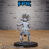 Rear view of the unpainted grey resin Amazoness Shaman miniature, showing the full feathered headdress splaying outward, segmented back armour, belted loincloth, claw-tipped boots, and the voodoo doll still visible hanging from the cord in her left hand, on a round 25.5mm base