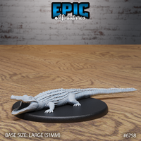 Unpainted grey resin alligator miniature by Epic Miniatures, front three-quarter view showing open jaws with visible teeth, detailed scute texture across the back, and four clawed feet on a large 51mm black oval base