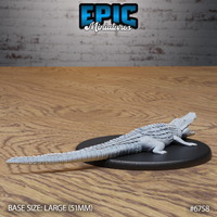 Unpainted grey resin alligator miniature by Epic Miniatures, rear three-quarter view showing the full length of the sculpt including the long tapered tail, dorsal scute detail, and hind legs on a large 51mm black oval base