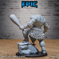 Rear view of the Blemmyes showing broad muscular back, feathered hide skirt, rope belt, and braided wrist bindings. The creature grips a large wooden club with both hands over a rocky scenic base. By Epic Miniatures.