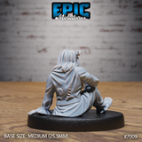 Tiefling figure seen from behind, seated, wearing ragged robes with a circular scar visible on the lower back and rough stitching along the seams. Long hair flows over the shoulders. Sculpt by Epic Miniatures.