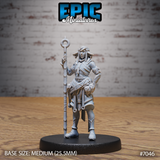 Firbolg Druid miniature facing forward, holding a tall staff with a ring finial raised in one hand, other hand on hip, wearing layered cloth wrappings with leaf-textured belt pouches. Sculpt by Epic Miniatures.
