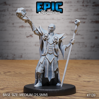 Skull-masked necromancer with arms raised wide, clutching a skull-topped orb aloft in one gauntleted hand and a tall staff with skull finial in the other, wearing angular bladed pauldrons adorned with circled skulls and long layered robes. Sculpt by Epic Miniatures.