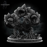 Front-facing digital render of the Hydra Bloom miniature by Stormborn Collectibles — a broad, root-legged plant creature with three large toothed flower-maws open wide, displayed against a dark stormy background, unpainted grey resin