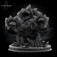 Front-facing digital render of the Hydra Bloom miniature by Stormborn Collectibles — a broad, root-legged plant creature with three large toothed flower-maws open wide, displayed against a dark stormy background, unpainted grey resin