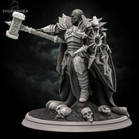 Three-quarter front angle of a bald warrior in sun-emblazoned armour raising an ornate warhammer overhead, large spiked shield at his side, skulls and rubble at his feet. Sculpt by Stormborn Collectibles.