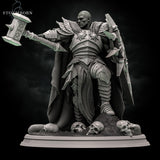 Rear view of an armoured warrior in layered plate with a heavy flowing cloak that drapes to the base, warhammer raised behind the shoulder, spiked pauldrons visible. Sculpt by Stormborn Collectibles.