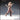 32mm resin render of Human Female Wizard 01 by Novaminis — three-quarter front view showing a dynamic mid-stride pose, one arm extended with pointing finger casting a spell, staff held low in the other hand, long flowing hair, utility belt with buckled pouches, and laced knee-high boots. Unpainted clay-tone render.
